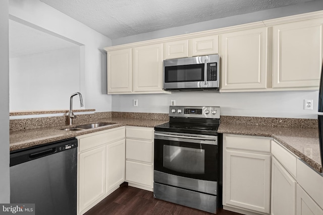 kitchen featuring sink, a textured ceiling, appliances with stainless steel finishes, dark hardwood / wood-style flooring, and dark stone counters