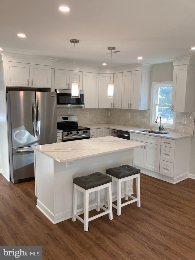 kitchen with pendant lighting, white cabinets, appliances with stainless steel finishes, a center island, and sink