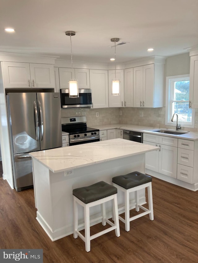 kitchen with decorative light fixtures, a center island, sink, white cabinetry, and appliances with stainless steel finishes