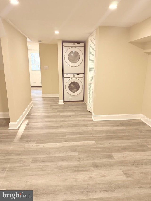 clothes washing area featuring light hardwood / wood-style flooring and stacked washing maching and dryer