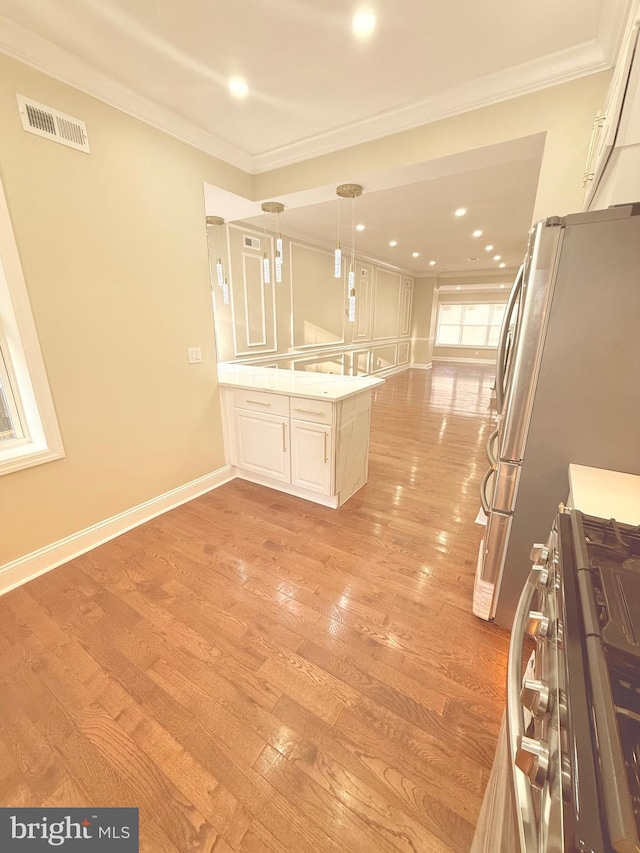 kitchen featuring kitchen peninsula, appliances with stainless steel finishes, decorative light fixtures, light wood-type flooring, and ornamental molding