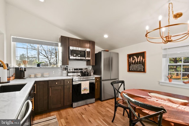 kitchen featuring stainless steel appliances, lofted ceiling, dark brown cabinets, and plenty of natural light