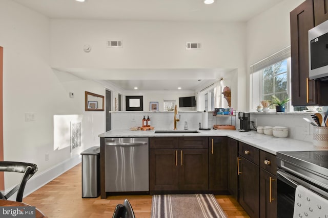 kitchen featuring tasteful backsplash, sink, dark brown cabinetry, stainless steel appliances, and light hardwood / wood-style flooring