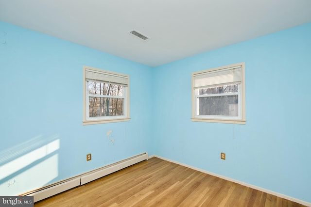 empty room featuring plenty of natural light, a baseboard heating unit, and light wood-type flooring