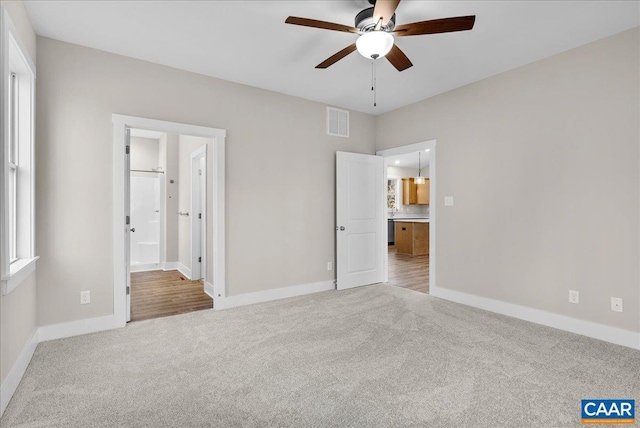 unfurnished bedroom featuring ceiling fan, light colored carpet, and ensuite bath