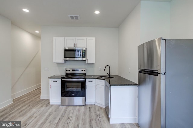 kitchen featuring white cabinets, stainless steel appliances, dark stone counters, sink, and light hardwood / wood-style flooring