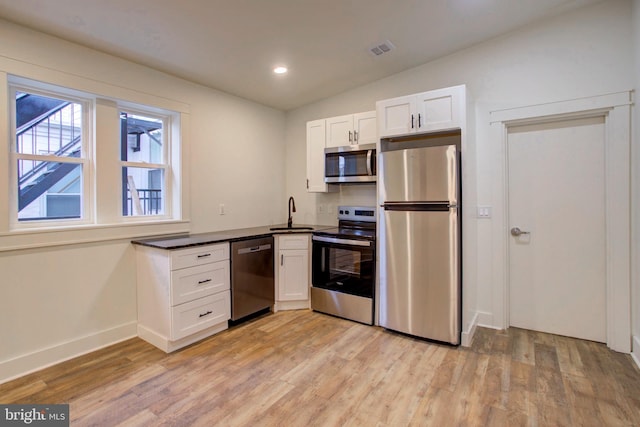 kitchen featuring lofted ceiling, white cabinets, light wood-type flooring, and stainless steel appliances