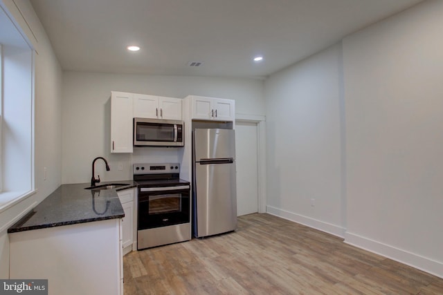 kitchen featuring appliances with stainless steel finishes, white cabinetry, dark stone counters, and sink