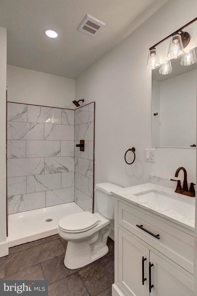 bathroom with toilet, tiled shower, and vanity