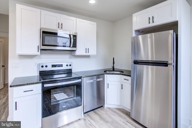 kitchen featuring light hardwood / wood-style floors, appliances with stainless steel finishes, dark stone counters, white cabinets, and sink