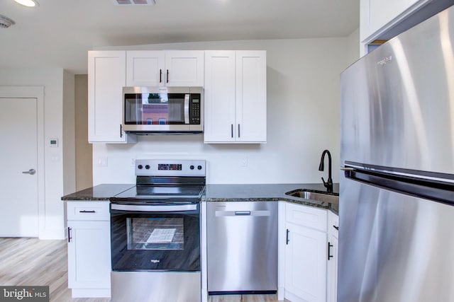 kitchen featuring appliances with stainless steel finishes, white cabinetry, dark stone counters, and sink