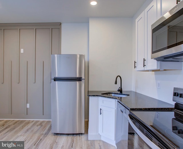 kitchen featuring appliances with stainless steel finishes, white cabinetry, dark stone countertops, sink, and light wood-type flooring