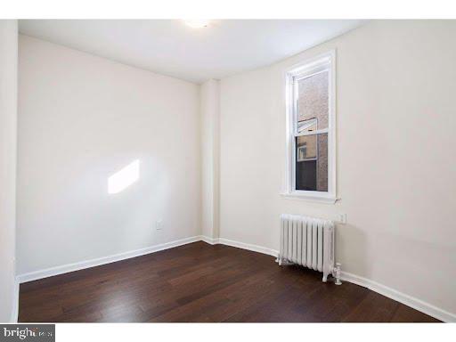 empty room featuring radiator heating unit and dark hardwood / wood-style flooring