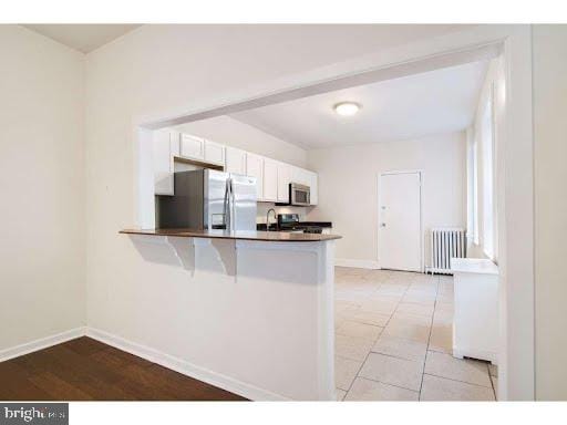 kitchen with radiator heating unit, appliances with stainless steel finishes, white cabinets, sink, and kitchen peninsula