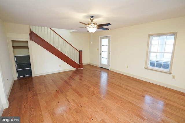 unfurnished living room with a ceiling fan, stairway, wood finished floors, and baseboards