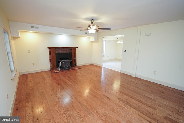 unfurnished living room with visible vents, ceiling fan with notable chandelier, light wood-style floors, baseboards, and a wood stove