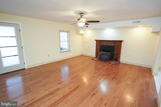 unfurnished living room with light wood finished floors, visible vents, baseboards, a wood stove, and a ceiling fan