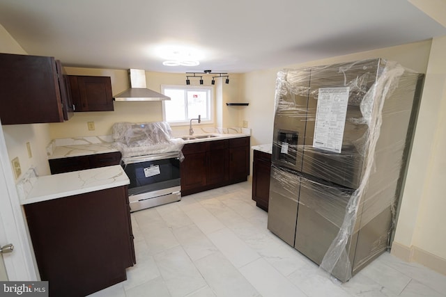 kitchen with light stone countertops, dark brown cabinetry, appliances with stainless steel finishes, wall chimney exhaust hood, and a sink