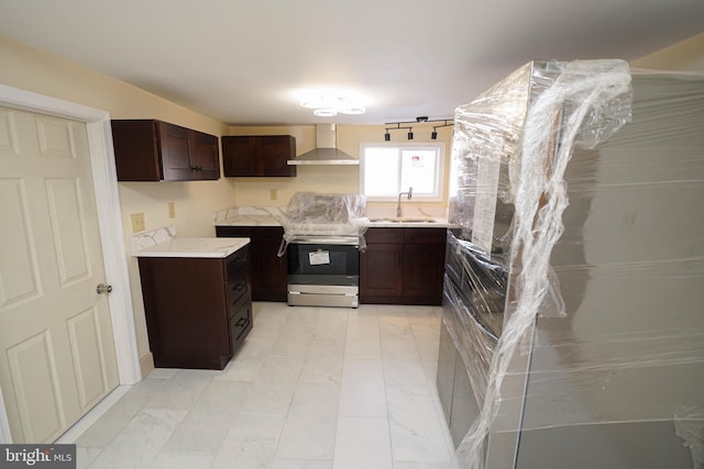 kitchen with dark brown cabinets, wall chimney range hood, stainless steel electric stove, light countertops, and a sink