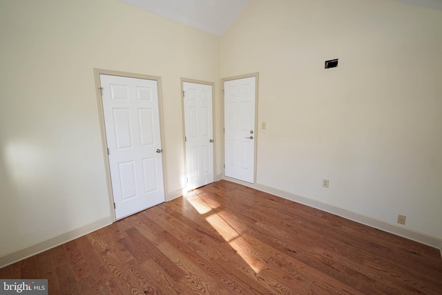 unfurnished bedroom featuring baseboards, high vaulted ceiling, and wood finished floors