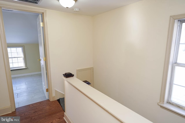 corridor with wood finished floors, an upstairs landing, visible vents, and baseboards