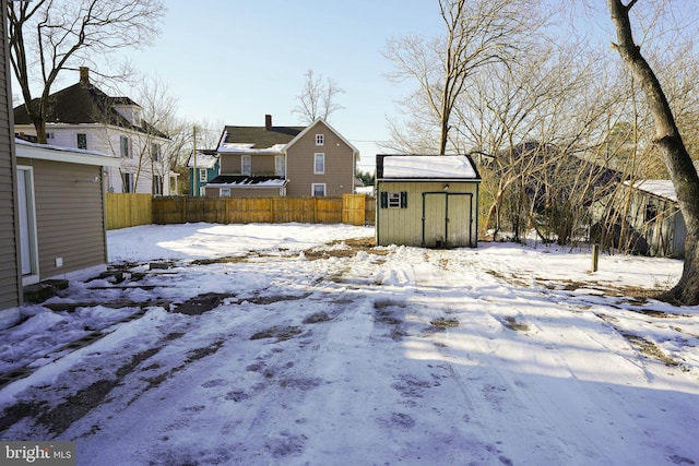 snowy yard featuring a storage unit, an outdoor structure, and fence