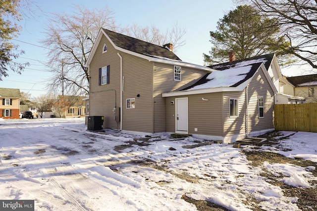 snow covered property featuring central air condition unit, a chimney, and fence