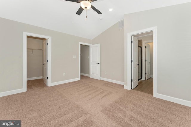 unfurnished bedroom with a spacious closet, lofted ceiling, a closet, ceiling fan, and light colored carpet