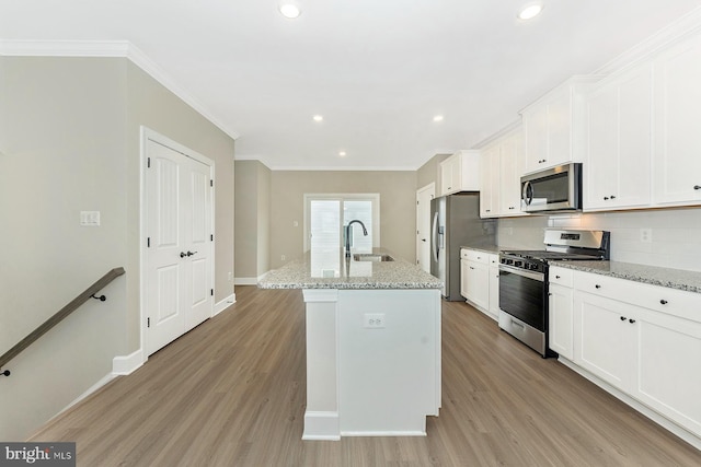 kitchen featuring a kitchen island with sink, backsplash, light stone counters, and stainless steel appliances