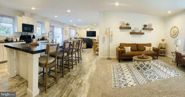 interior space featuring a kitchen bar, white cabinets, black appliances, and a center island with sink