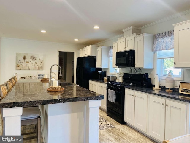 kitchen with white cabinetry, black appliances, dark stone counters, and an island with sink