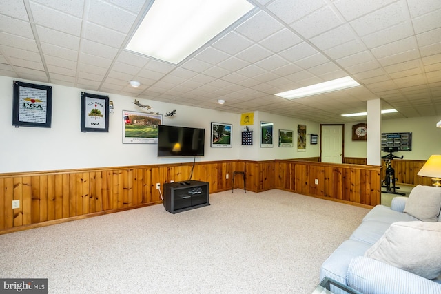 carpeted living room featuring a paneled ceiling and wood walls