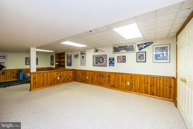 basement with carpet, a paneled ceiling, and wood walls