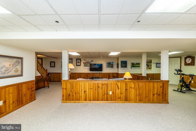 kitchen with a paneled ceiling, light colored carpet, and wood walls