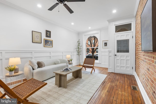 living room with light hardwood / wood-style floors, brick wall, crown molding, and ceiling fan