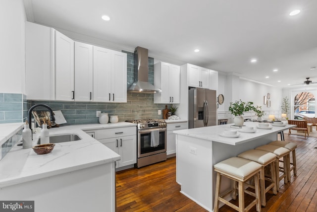 kitchen with wall chimney range hood, a kitchen island, white cabinetry, light stone countertops, and stainless steel appliances