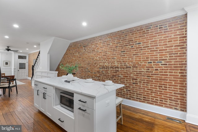 kitchen with a center island, white cabinetry, light stone countertops, a kitchen breakfast bar, and brick wall