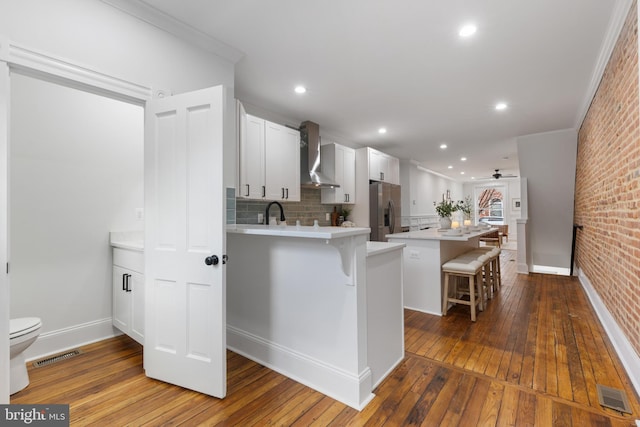 kitchen with stainless steel fridge, brick wall, wall chimney exhaust hood, white cabinets, and a breakfast bar