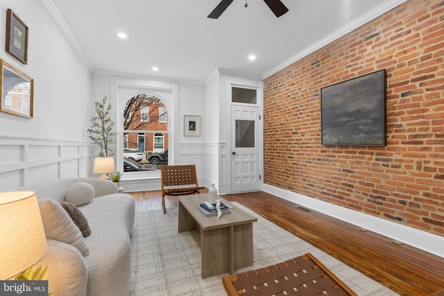 living room featuring ceiling fan, brick wall, and ornamental molding