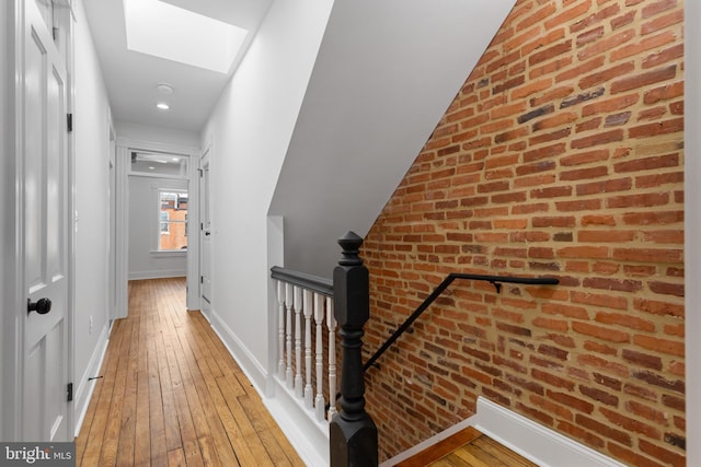 hallway with hardwood / wood-style flooring, brick wall, and a skylight