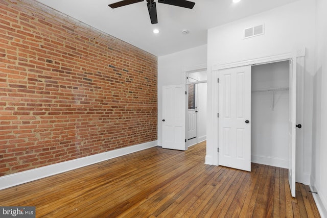 unfurnished bedroom with ceiling fan, brick wall, a closet, and dark hardwood / wood-style floors