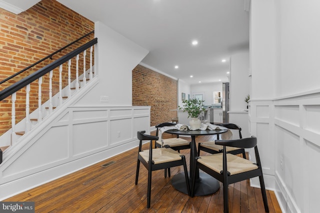 dining area featuring brick wall, ornamental molding, and hardwood / wood-style floors