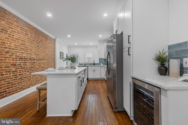 kitchen with a breakfast bar, beverage cooler, white cabinets, stainless steel fridge, and brick wall