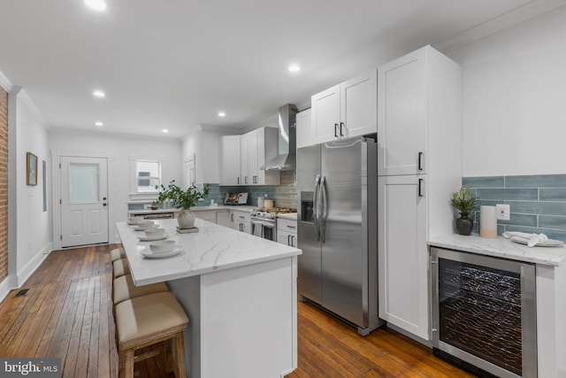 kitchen with white cabinetry, stainless steel appliances, wine cooler, wall chimney exhaust hood, and a center island