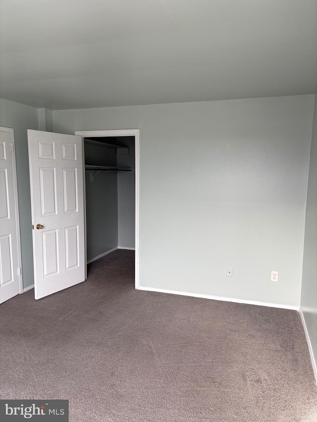 unfurnished bedroom featuring dark carpet and a closet