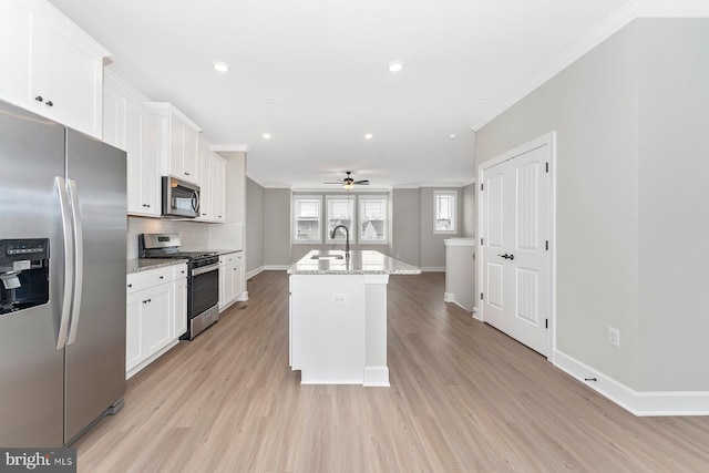 kitchen featuring light stone countertops, appliances with stainless steel finishes, an island with sink, and white cabinetry