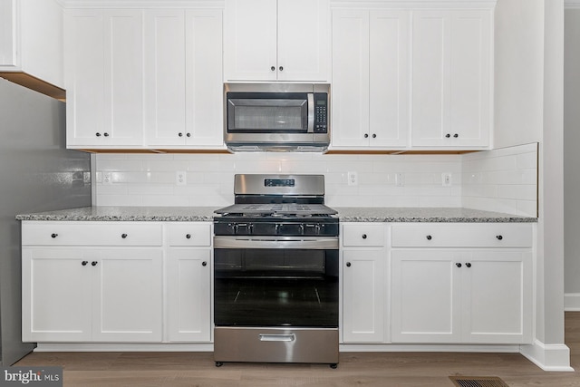 kitchen with tasteful backsplash, light stone countertops, stainless steel appliances, and white cabinetry