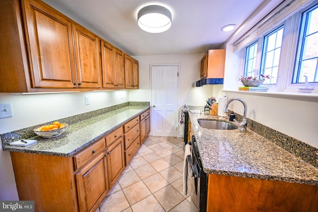 kitchen featuring sink, stainless steel stove, light tile patterned flooring, black dishwasher, and dark stone countertops