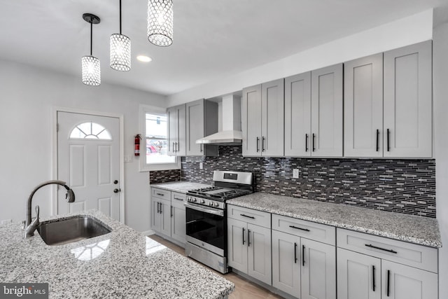 kitchen featuring sink, stainless steel range with gas cooktop, pendant lighting, light stone countertops, and wall chimney range hood