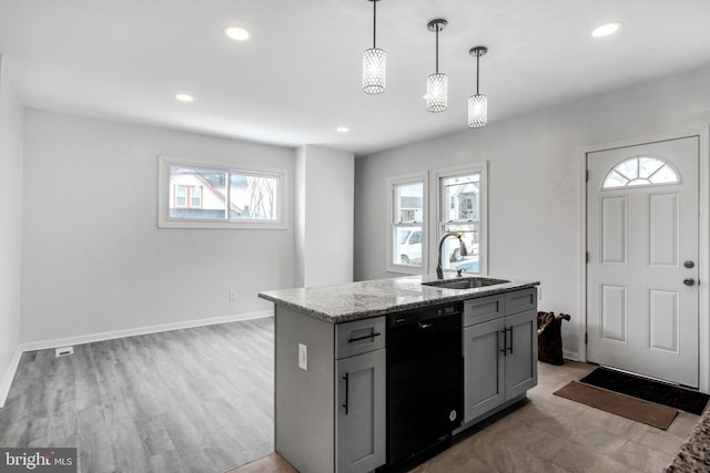 kitchen with decorative light fixtures, dishwasher, an island with sink, sink, and light stone counters